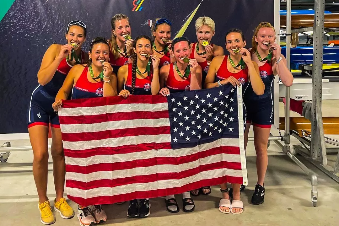 Jordan Hyde '25 and the rest of the women's eight bite their gold medals behind an American flag at the Wolrd University Games